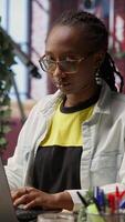 Vertical Portrait of cheerful woman in home office opening laptop, starting working on tasks. Joyous african american person using electronic notebook device to do job online, camera B video