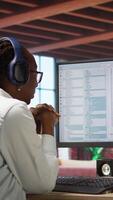 Vertical Jolly engineer in home office working on computer, dancing at desk in celebration after successfully executing code. IT worker wearing headphones happy after finishing compiling code, camera A video
