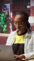 Vertical Portrait of cheerful woman in home office opening laptop, starting working on tasks. Joyous african american person using electronic notebook device to do job online, camera A video