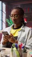 Vertical Happy woman relaxing in apartment, texting friends on smartphone, enjoying leisure time. Smiling person taking break from studying to talk with mates on social media website using phone, camera A video