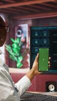 Vertical Woman using isolated screen smartphone and AI LLM chatbot on computer screen in home office. Person holding chroma key phone uses artificial intelligence chatbot on monitor, camera A video