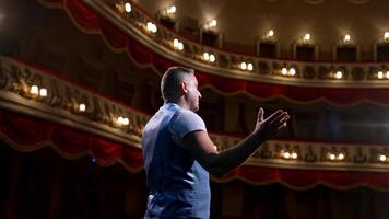 Kyiv, Ukraine, 29 May 2024 Presenter in front of empty theatre hall with red velvet chairs. Actor is standing on stage and talking with gestures before the performance. video