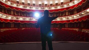 Kyiv, Ukraine, 2 May 2024 Man in front of empty theatre hall with red velvet chairs. Actor is standing on stage and talking with gestures before the performance. video
