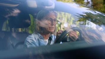 Shocked upset frustrated Caucasian senior mature pensioner in glasses female woman car automobile driver inside vehicle using mobile phone app smartphone shock failure losing error hit steering wheel video