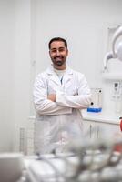 vertical Portrait of smiling dentist posing with crossed arms in his clinic photo