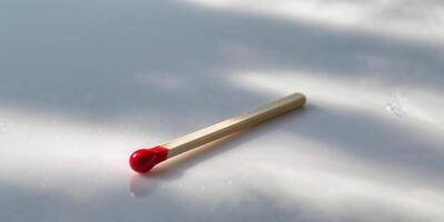Single safety matchstick with a vibrant red tip resting on a white surface in soft lighting photo