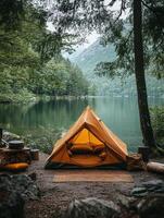 A cozy orange tent by a serene lake surrounded by trees, ideal for camping and relaxation. photo