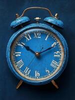 A vintage blue alarm clock with a distressed finish, displaying Roman numerals and two bells. photo