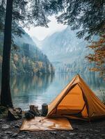 A serene camping scene by a lake with a yellow tent surrounded by trees and mountains. photo
