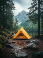 A vibrant yellow tent by a serene lake, surrounded by lush forests and mountains. photo