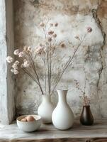 A serene arrangement of vases with dried flowers and a bowl of fruit on a rustic surface. photo