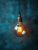A glowing vintage light bulb hanging against a textured blue backdrop. photo