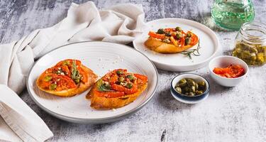 Appetizing bruschetta with dried tomatoes and pickled capers on a plate on the table web banner photo