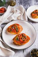 Italian crostini with sun-dried tomatoes, capers and spices on a plate on a table vertical view photo