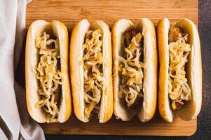 Close up of hot dogs with caramelized onions on a board on a table top view photo