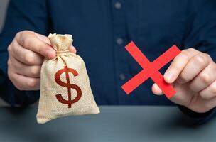 Man holding red cross and dollar money bag. Refusal to grant a loan. Failure to return the collateral. Refusal of sale and cooperation. Risk of confiscation of funds. photo