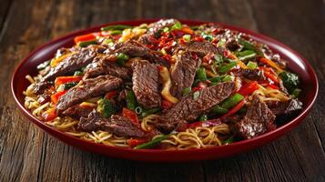 Stir-fried beef and vegetable noodles served in a red bowl photo