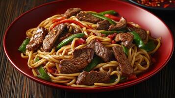 Savory stir-fried beef and noodles with vegetables in a red bowl photo