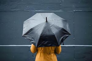 Rainy Day Solitude. A Person Under a Black Umbrella During a Gentle Rain, Wearing a Yellow Coat Against a Dark Gray Background, Evoking Feelings of Calm and Introspection. photo