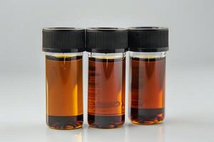 Amber Liquid Samples in Glass Vials. A Close-Up Examination of Three Containers Filled with a Translucent, Golden-Brown Substance, Showing Detailed Textures and Reflections on a Light Background. photo