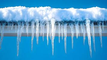 Long icicles hang from roof edge against crystal clear blue sky, displaying frozen water droplets and transparent ice formation with dramatic natural lighting in winter scene. sky photo