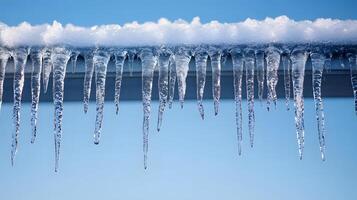 Long icicles hang from roof edge against crystal clear blue sky, displaying frozen water droplets and transparent ice formation with dramatic natural lighting in winter scene. transparent photo