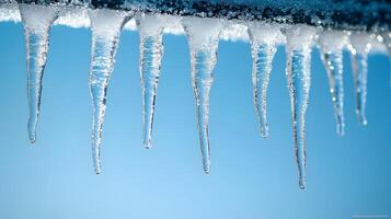 Long icicles hang from roof edge against crystal clear blue sky, displaying frozen water droplets and transparent ice formation with dramatic natural lighting in winter scene. frost photo