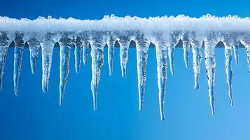 Long icicles hang from roof edge against crystal clear blue sky, displaying frozen water droplets and transparent ice formation with dramatic natural lighting in winter scene. winter photo