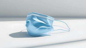 Simple blue surgical mask illustration floats against pure white background. Clean design emphasizes medical protection with subtle shadow beneath disposable face covering. minimal photo