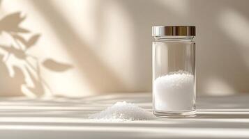Traditional glass salt shaker displays white crystals through clear container. Metal cap with holes tops minimalist design, captured with soft window lighting and gentle shadows. culinary photo