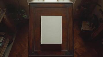 A solitary, blank book rests on a polished wooden table in soft light photo