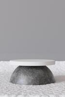Modern product display podium with stone-textured base and white circular top on a snowy background with a neutral gray wall. Ideal for showcasing products in a minimalistic winter setting. 3D render. photo