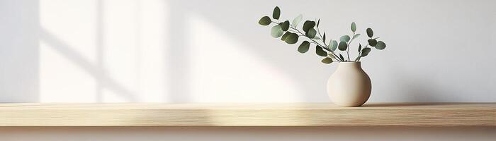 A light oak wooden shelf displays a soothing matte ceramic vase in beige, adorned with a sprig of eucalyptus. This calming setup enhances a minimalist aesthetic against a soft wall backdrop photo
