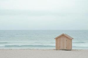 A small wooden beach hut sits quietly on a smooth sandy beach, surrounded by soft waves and a calming atmosphere, perfect for relaxation and contemplation photo