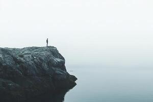 A solo hiker stands on a rocky cliff, absorbing the peaceful atmosphere of a Nordic fjord. Muted tones enhance the sense of tranquility and adventure in this breathtaking location photo
