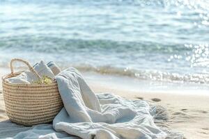 A light linen blanket and a woven basket with pastel-colored items are placed on a serene shoreline. Soft waves lap gently, creating a tranquil atmosphere perfect for unwinding photo
