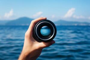 A person holding up a camera lens with a view of the ocean photo