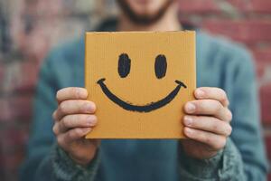 Person holding a cheerful box with a smiley face against a textured brick wall during daylight photo
