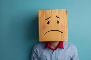 A person with a box on their head expressing sadness, posing against a blue wall in a lighthearted indoor setting photo