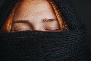 A woman with freckled skin and red hair is wrapped in a black shawl, eyes closed in peaceful contemplation against a dark background photo