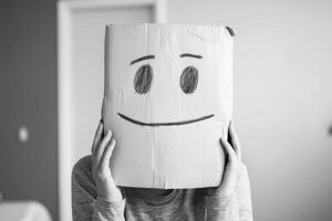 A person wearing a cardboard box with a smiley face while sitting in a minimalistic indoor space photo