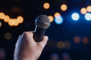 A hand holding a microphone in a dimly lit venue with bright lights during a live performance or speech event photo