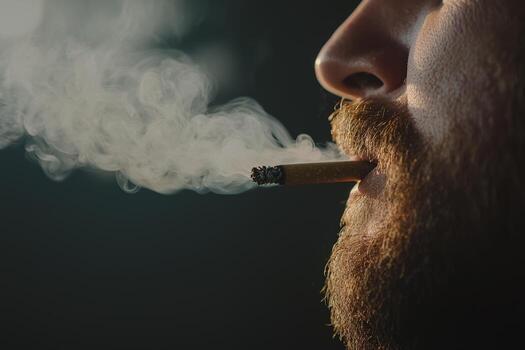Man exhaling smoke from a cigarette in a dimly lit environment during late evening hours photo