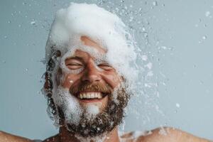 Man enjoying a bubbly foam bath indoors, smiling joyfully while water splashes around him against a light blue background photo