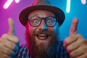 A joyful man expresses excitement with a big smile and thumbs up, wearing glasses and a hat, surrounded by colorful neon lights in a lively setting. photo