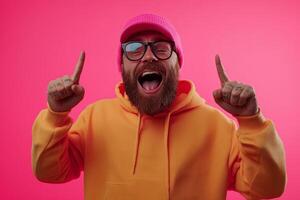 A joyful man wearing a pink beanie and orange hoodie celebrates with a bright smile against a vivid pink background photo