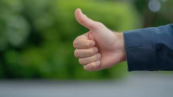 Hand Giving Thumbs Up Gesture Outdoors Showing Approval, Focus on Right Hand Against Blurred Green Background, Wearing Dark Jacket, Symbolizing Positive Feedback, Agreement, Supportive Gesture photo