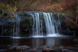Long exposure of a waterfall flowing over mossy rocks in a tranquil autumn forest photo