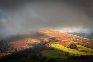 Sunlight filtering through clouds illuminating colorful autumn hills photo
