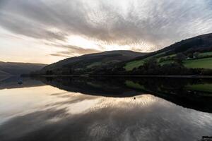 Calm lake reflecting green hills and cloudy sky at sunset photo